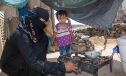 A young, displaced mother cooking food for her child at a displacement site in Ma’rib ©IOM 2021/ E. Al Oqabi